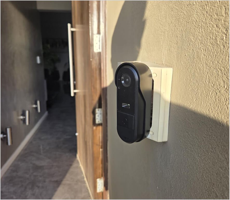 Customer photo of a Vital Smart Door Home doorbell camera installed on a textured wall beside a wooden front door